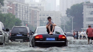 Árvízi hajós az autó tetején egy kínai nagyváros kellős közepén